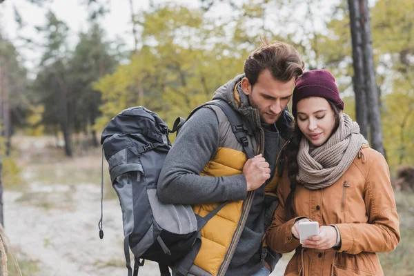 Pareja de turistas jóvenes mirando el teléfono inteligente mientras busca la dirección en el bosque - foto de stock