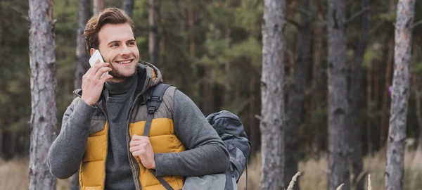 Sonriente turista hablando por teléfono móvil mientras camina en el bosque de otoño, bandera - foto de stock