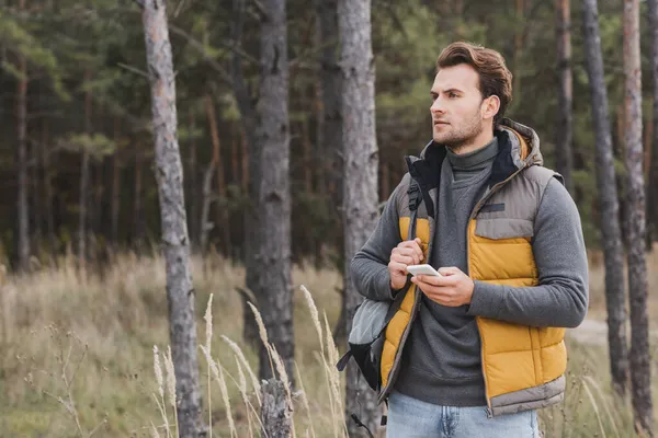 Молодий мандрівник з рюкзаком тримає мобільний телефон під час походу в ліс — стокове фото