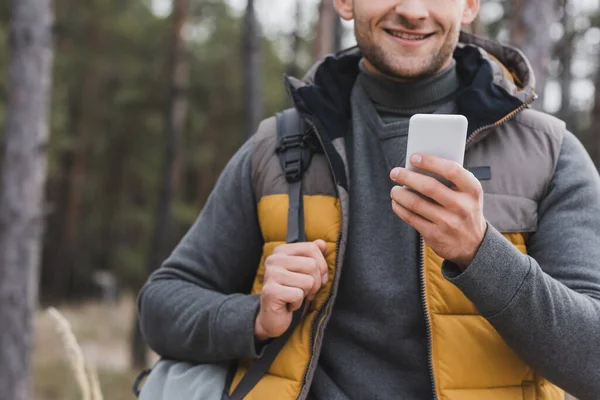 Partial view of man with backpack using smartphone for navigation in forest — Stock Photo