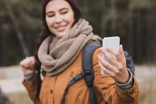Розмита жінка посміхається, приймаючи селфі на мобільний телефон на відкритому повітрі — стокове фото