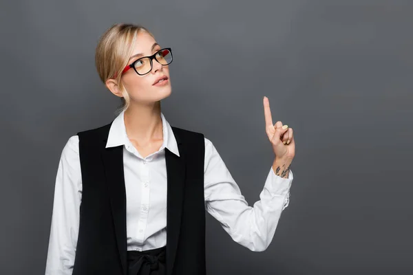 Young businesswoman in white shirt and eyeglasses pointing with finger isolated on grey — Stock Photo