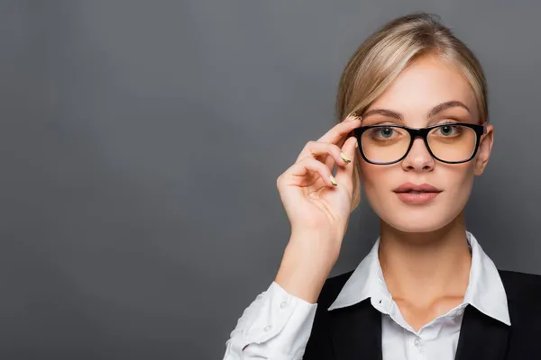 Blonde businesswoman holding eyeglasses while looking at camera isolated on grey — Stock Photo
