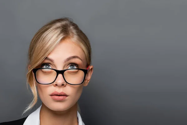 Білявка бізнес-леді в окулярах дивиться вгору ізольовано на сірий — стокове фото