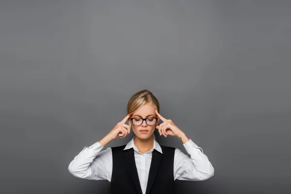 Femme d'affaires pensive dans des lunettes tenant les doigts près de la tête sur fond gris — Photo de stock