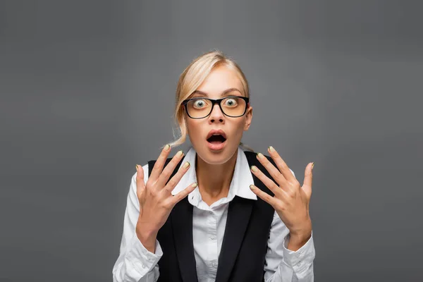 Shocked businesswoman in eyeglasses looking at camera isolated on grey — Stock Photo