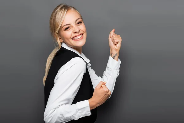 Happy blonde businesswoman in shirt and vest looking at camera on grey background — Stock Photo