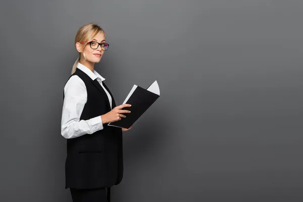 Junge Geschäftsfrau mit Brille blickt in die Kamera, während sie eine Papiermappe in Grau hält — Stockfoto