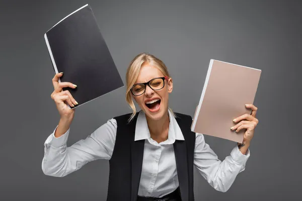 Stressed businesswoman holding paper folders while screaming isolated on grey — Stock Photo