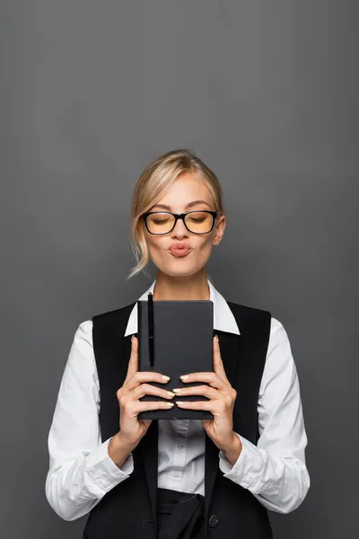 Blonde Geschäftsfrau mit Brille schmollen Lippen und halten Notizbuch isoliert auf grau — Stockfoto