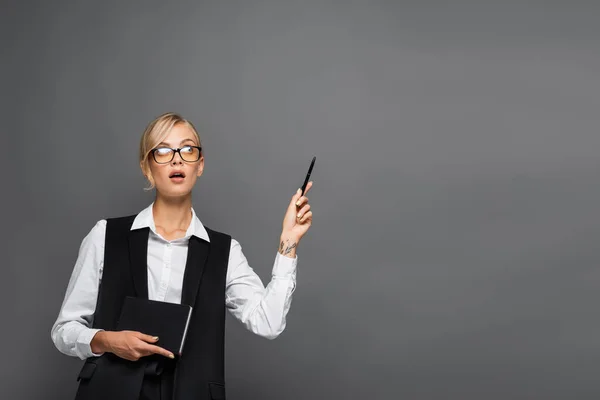 Umsichtige Geschäftsfrau hält Notizbuch in der Hand und zeigt mit der Hand isoliert auf Grau — Stockfoto