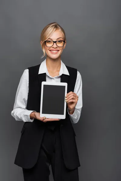 Positive Geschäftsfrau mit Brille hält digitales Tablet mit leerem Bildschirm isoliert auf grau — Stockfoto