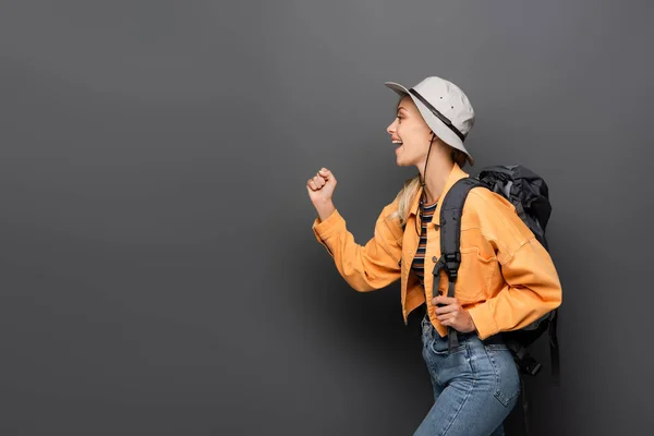 Side view of cheerful traveler with backpack showing yes gesture on grey background — Stock Photo