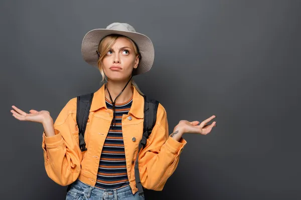 Turista pensativo en sombrero mostrando gesto de encogimiento aislado en gris - foto de stock