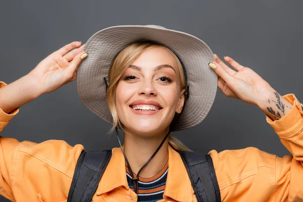Portrait of cheerful tourist holding hat and looking at camera isolated on grey — Stock Photo
