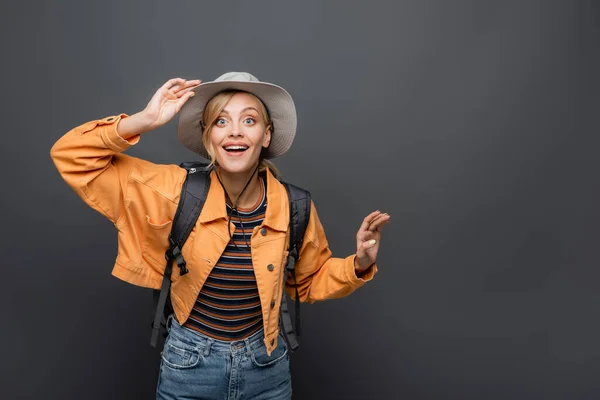 Emocionado viajero con sombrero y mochila mirando a la cámara aislada en gris - foto de stock