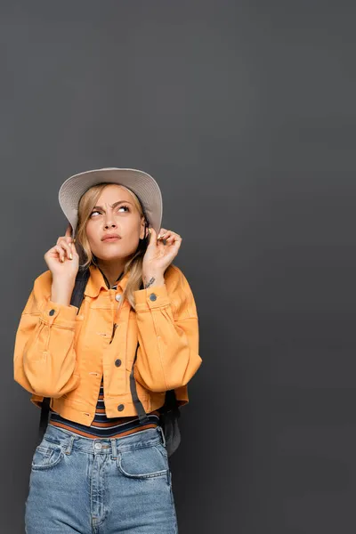 Scared tourist with backpack holding hat isolated on grey — Stock Photo