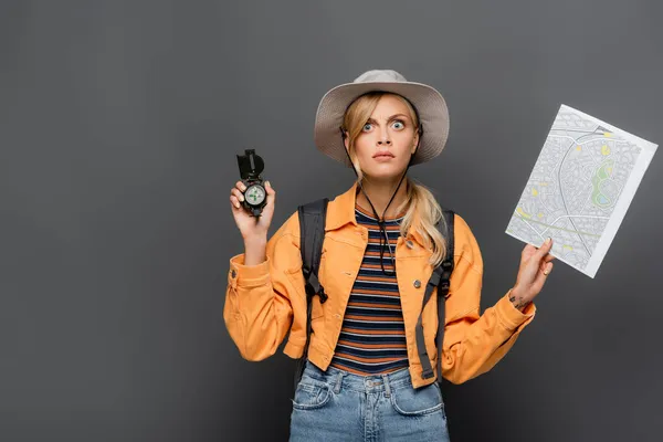 Viajante atencioso com mochila segurando bússola e mapa isolado em cinza — Fotografia de Stock