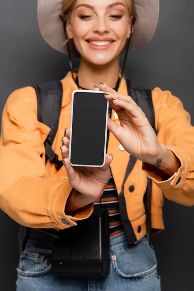 Smartphone con pantalla en blanco en manos de turista alegre borrosa sobre gris - foto de stock