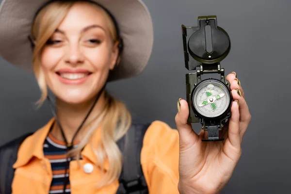 Kompass in der Hand eines verschwommenen lächelnden Touristen isoliert auf grau — Stockfoto