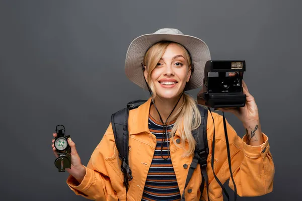 Веселый путешественник держит винтажную камеру и компас, изолированный на сером — стоковое фото