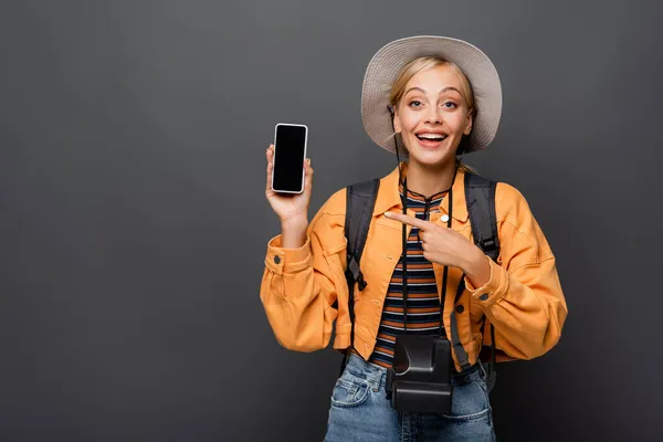 Positiver Tourist mit Oldtimer-Kamera, die auf Smartphone auf grauem Hintergrund zeigt — Stockfoto