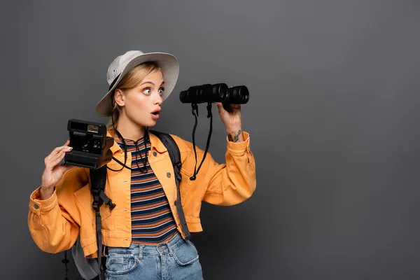 Verblüffter Tourist mit Oldtimer-Kamera blickt auf Fernglas isoliert auf grau — Stockfoto