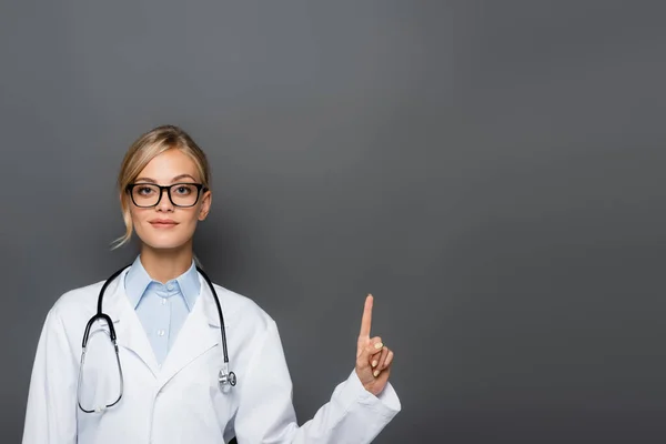 Jeune médecin en manteau blanc pointant avec doigt isolé sur gris — Photo de stock