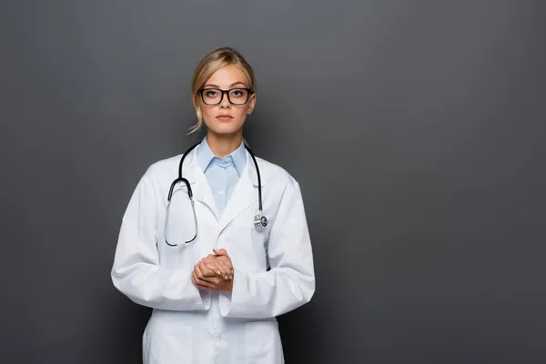 Блондинка лікар в окулярах дивиться на камеру ізольовано на сірому — стокове фото