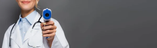 Vista cortada do pirômetro na mão de médico borrado isolado em cinza, banner — Fotografia de Stock