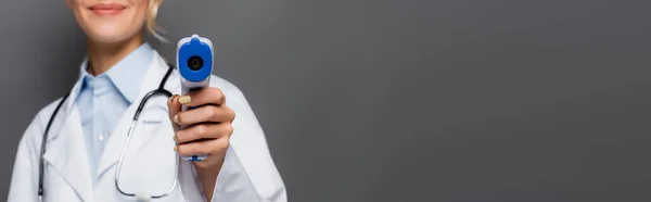 Vue recadrée du pyromètre en main du médecin flou isolé sur gris, bannière — Photo de stock