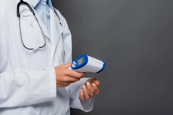 Cropped view of doctor holding non contact pyrometer isolated on grey — Stock Photo