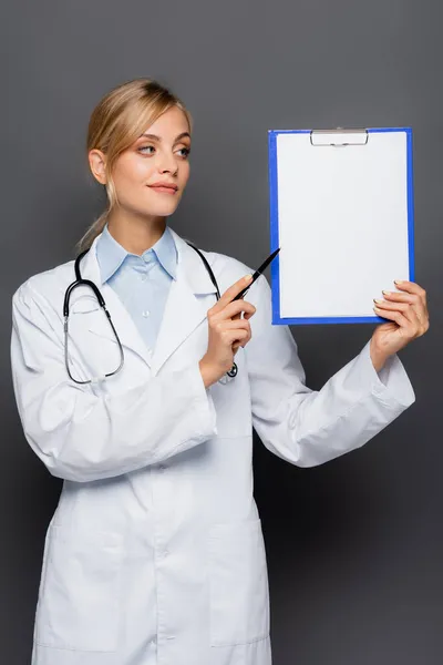 Young doctor pointing at clipboard with copy space isolated on grey — Stock Photo