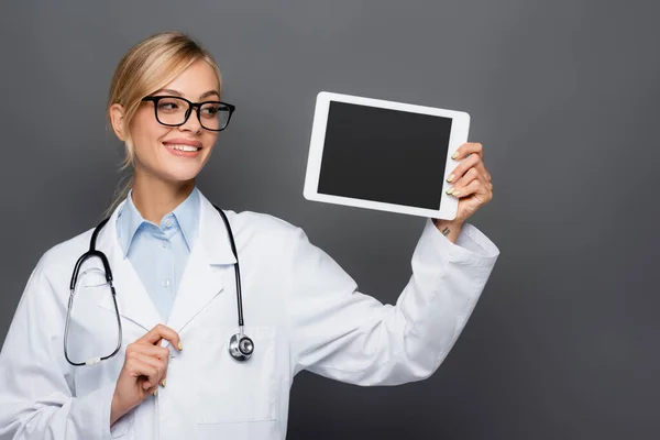 Médecin blond souriant regardant la tablette numérique avec écran blanc isolé sur gris — Photo de stock