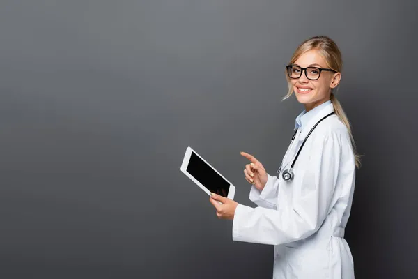 Позитивний лікар вказує на цифровий планшет з порожнім екраном ізольовано на сірому — стокове фото