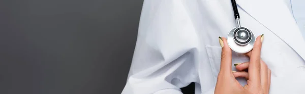 Cropped view of doctor in white coat holding statoscope isolated on grey, banner — Stock Photo