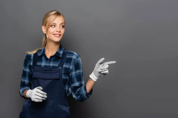 Encanador sorridente em luvas apontando com o dedo no cinza — Fotografia de Stock