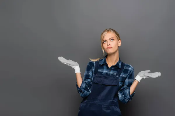 Plomero pensativo en guantes mirando hacia otro lado sobre fondo gris - foto de stock