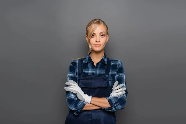 Blonde plumber in gloves standing with crossed arms isolated on grey — Stock Photo