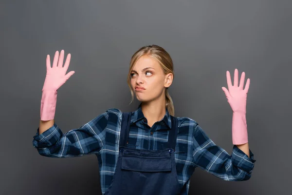 Fontanero disgustado en overol mirando las manos con guantes de goma aislados en gris - foto de stock