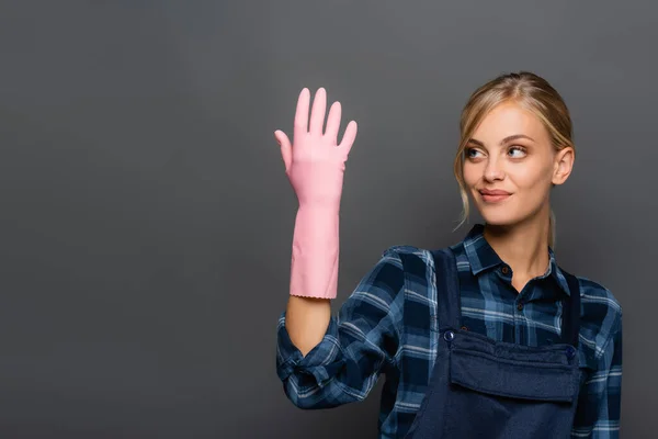 Plombier blonde souriante regardant la main en gant de caoutchouc isolé sur gris — Photo de stock