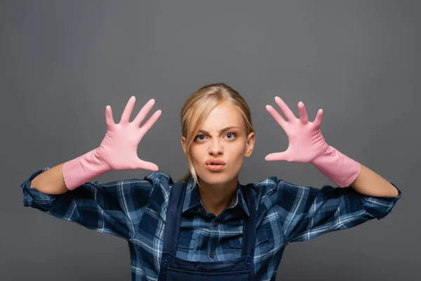 Disgusted plumber in rubber gloves gesturing and looking at camera isolated on grey — Stock Photo