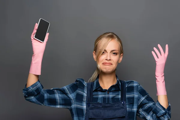 Aufgebrachte Klempner in Overalls und Gummihandschuhen halten Smartphone mit leerem Bildschirm isoliert auf grau — Stockfoto