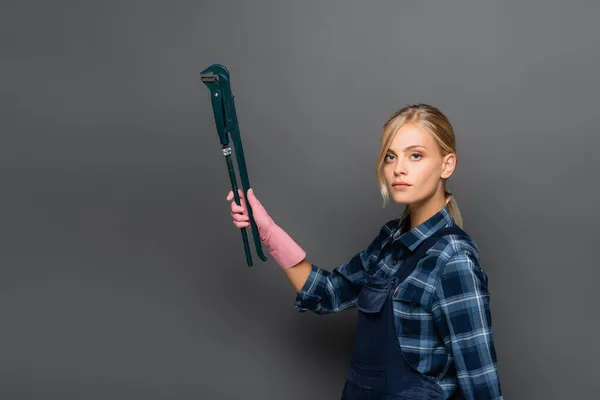 Blonde Klempner mit Rohrschlüssel und Blick in die Kamera auf grauem Hintergrund — Stockfoto