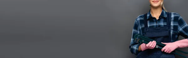 Vista cortada de loira reparadora em luvas de borracha segurando chave de tubo isolado em cinza, banner — Fotografia de Stock