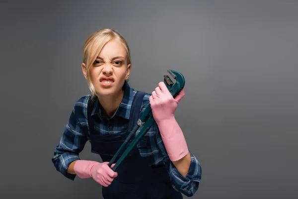 Angry plumber in overalls holding pipe wrench and looking at camera isolated on grey — Stock Photo