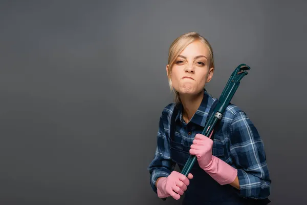 Irritated plumber in rubber gloves holding pipe wrench isolated on grey — Stock Photo