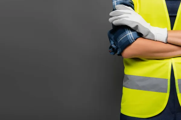 Vista ritagliata del giovane costruttore in giubbotto di sicurezza incrocio braccia isolato su grigio — Foto stock