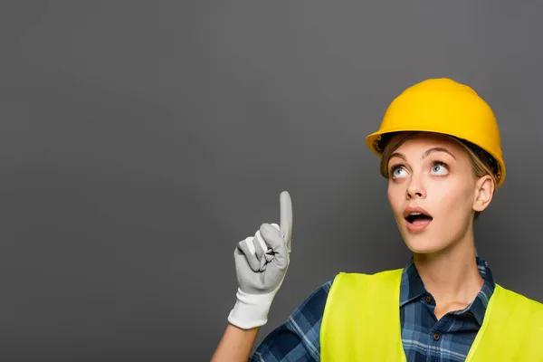 Amazed builder in safety vest having idea isolated on grey — Stock Photo