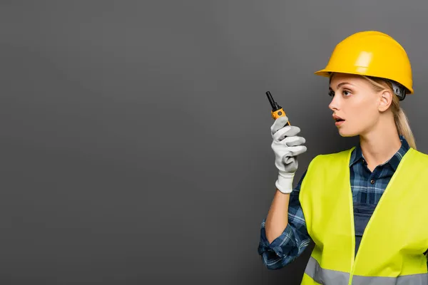 Rubia constructora en guante y chaleco de seguridad usando walkie talkie aislado en gris - foto de stock